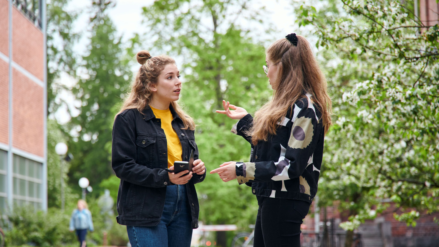 kaksi opiskelijaa juttelemassa kampusalueella ulkona