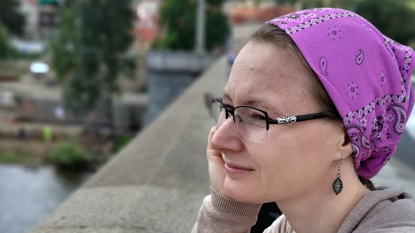 Tatiana leaning to a banister. She has brown hair, purple beanie and glasses.