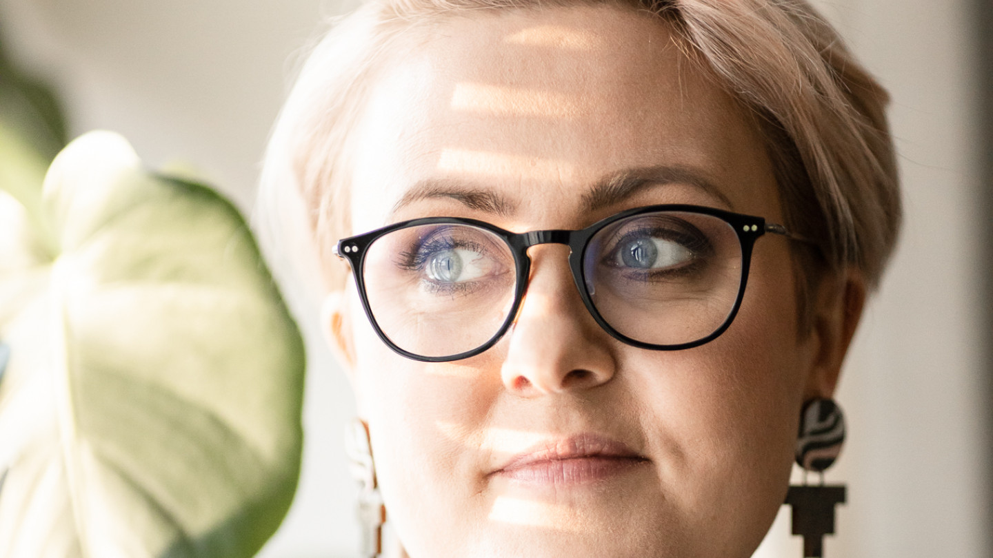 Anna Haverinen, jolla on vaaleat lyhyet hiukset ja silmälasit. Hän on kuvattuna peikonlehden edessä.