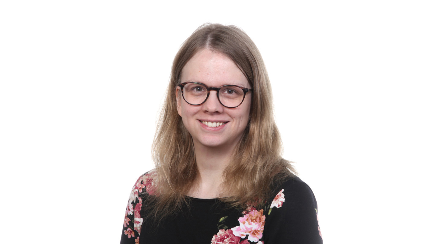 Sara AlaHynnilä, jolla on vaaleanruskeat puolipitkät hiukset ja silmälasit. Yllään hänellä on musta paita, jossa on ruusukuvioita.