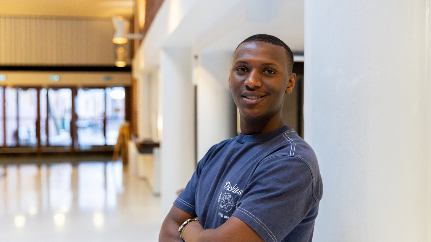 Opiskelijalähettiläs seisoo yliopiston käytävällä, katsoo kameraan ja hymyilee