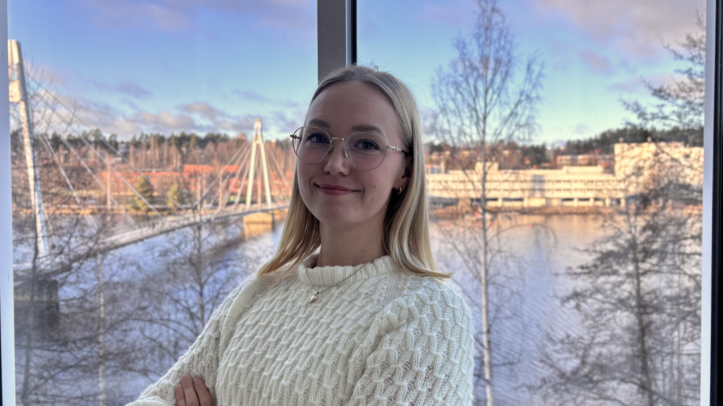 Hanna katsoo kameraan hymyillen. Hänellä on vaaleat hiukset ja silmälasit. 