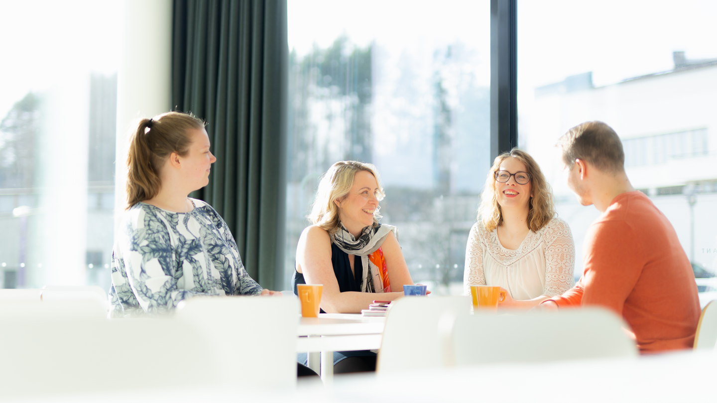 Neljä hymyilevää ihmistä keskustelevat