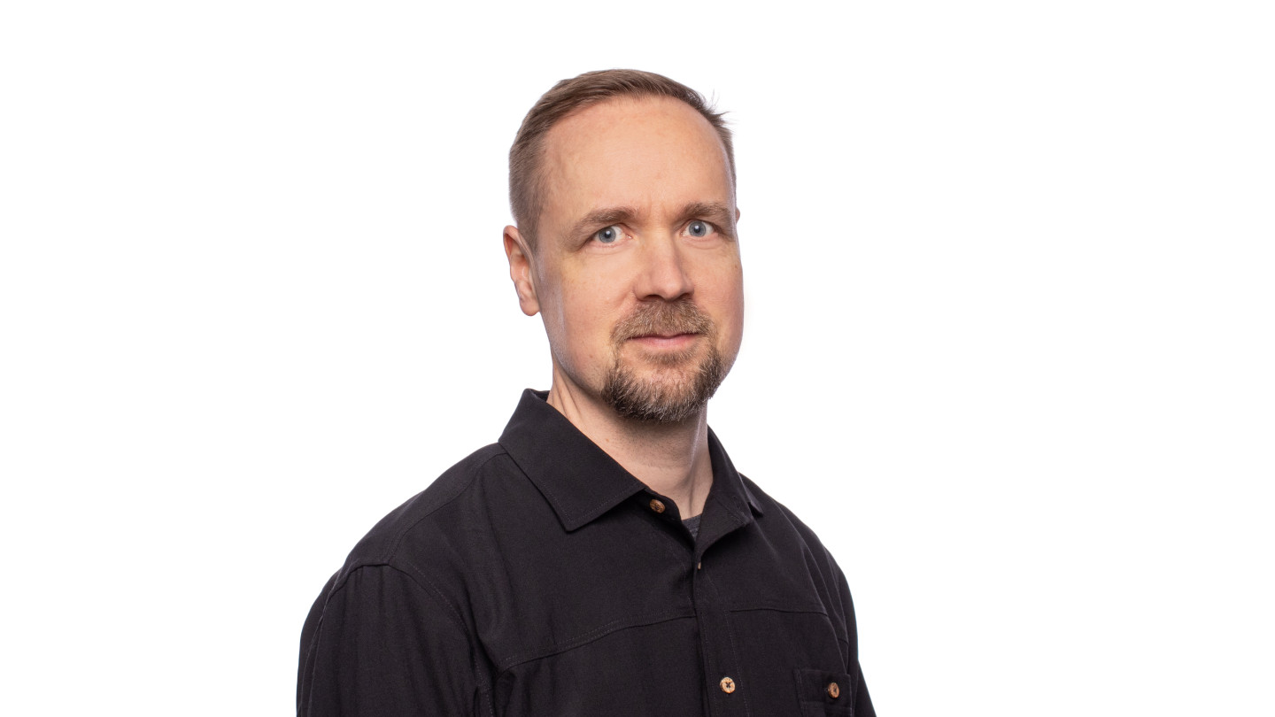 Henkilö katsoo kameraan. Musta kauluspaita päällä.