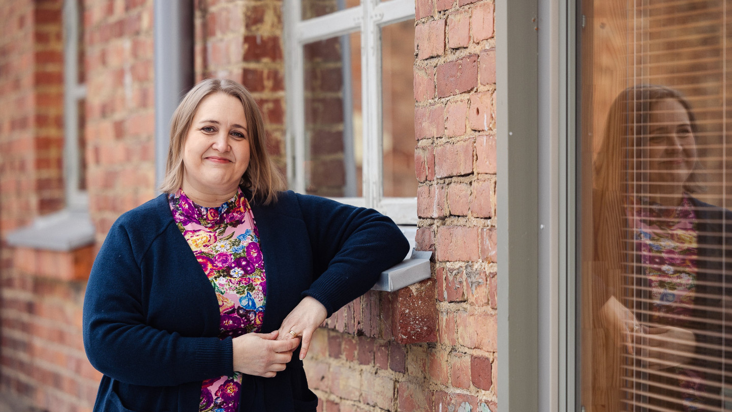 Henkilö nojaa kyynärpäällään punatiilitalon ikkunalautaan