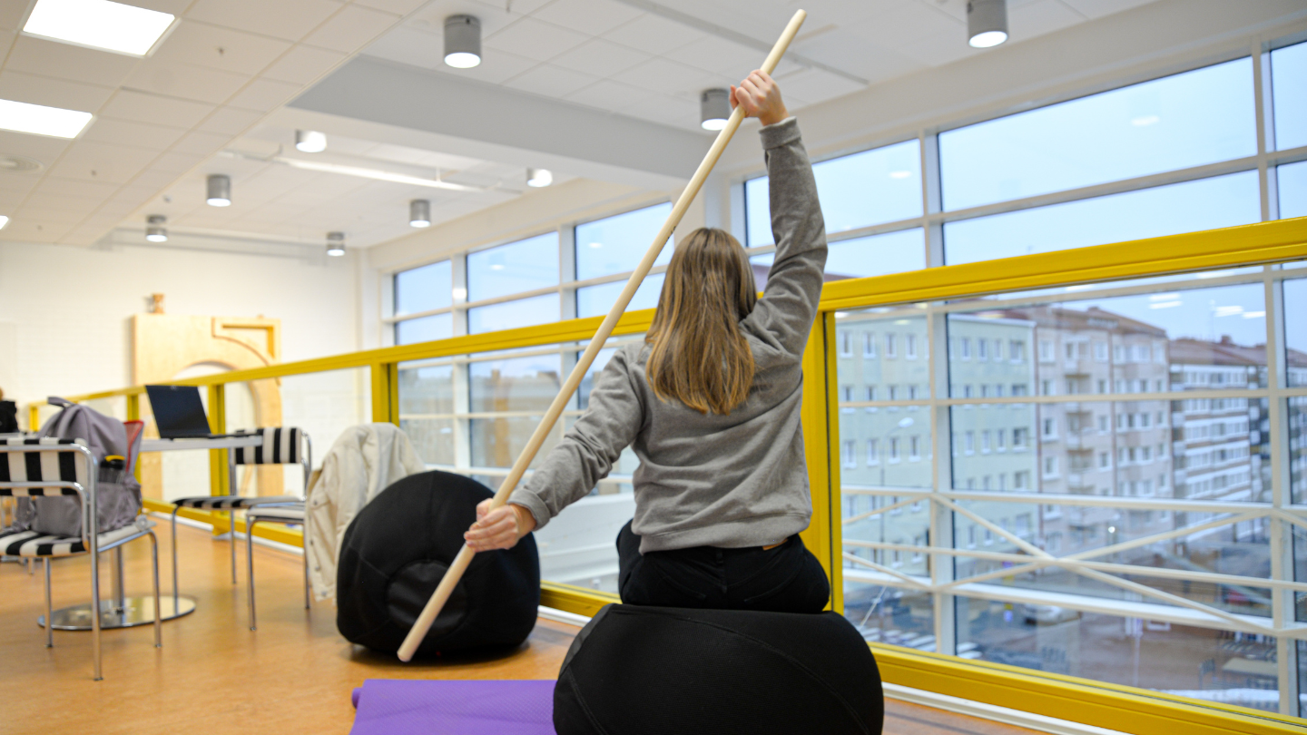A student stretches with an exercise stick in the activation corner of Lähde.