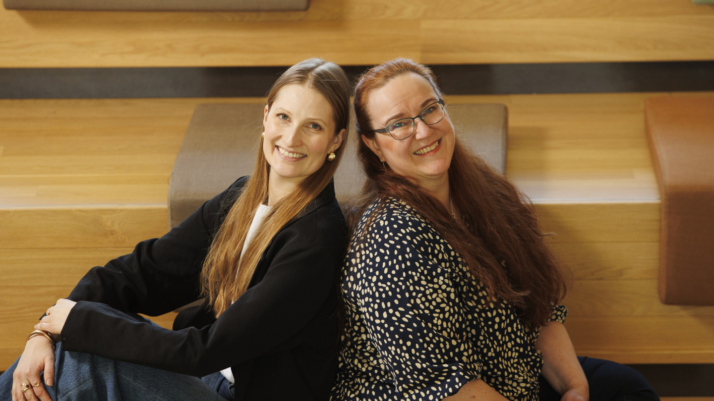 Taru Lilja ja Johanna Rantanen istuvat yhdessä ja hymyilevät kameralle.