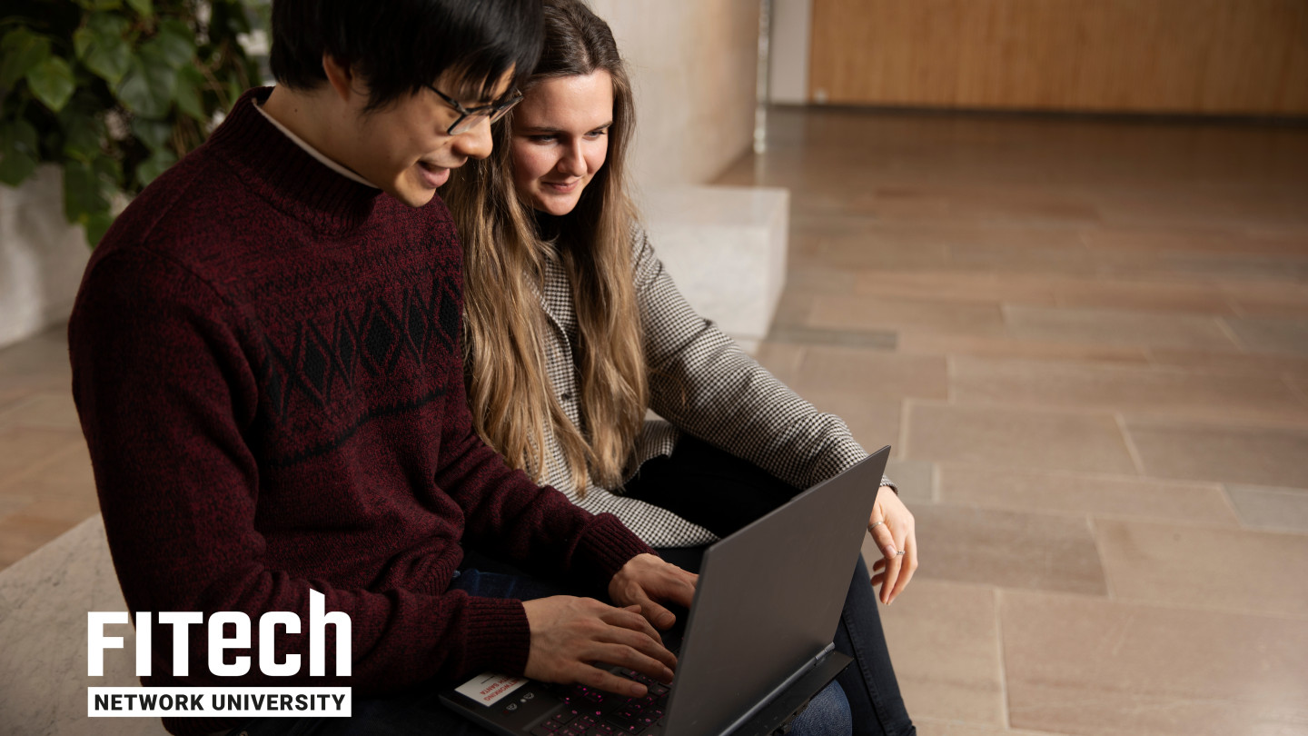 Mies ja nainen istuvat penkillä, mies on tietokoneen äärellä ja nainen seuraa vierestä