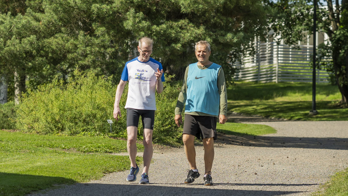 Kaksi henkilöä kävelee puistotietä