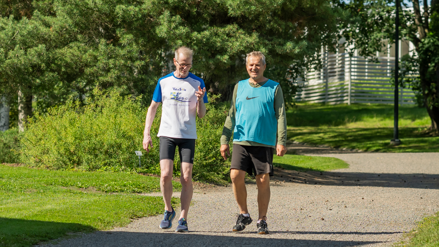 Kaksi henkilöä kävelee puistotietä