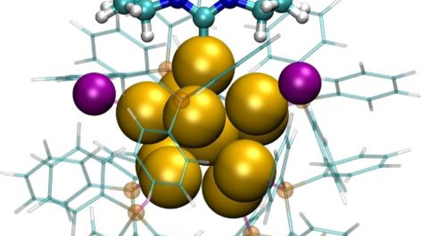 Jyväskylän yliopiston nanotiedekeskuksen simulaatioissa ennustettu yhdentoista kultaatomin (keltaiset pallot) nanohiukkanen, jonka pinnalla on suojaavia molekyylejä. Kuvan yläosan molekyyli on karbeeni, violetit pallot klooreja ja muut molekyylit fosfiineja. Visualisointi: Sami Kaappa, Jyväskylän yliopisto
