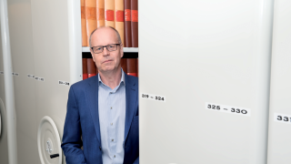 Jarmo avonaisen arkistohyllyn edessä, yllään hänellä on sininen pikkutakki.