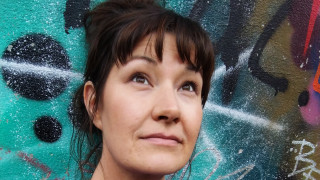 Satu Hotari, jolla on tumman ruskeat puolipitkät hiukset ponnarilla. Hän seisoo graffitin edessä.