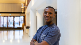 Opiskelijalähettiläs seisoo yliopiston käytävällä, katsoo kameraan ja hymyilee