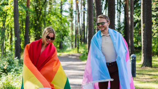 Kaksi henkilöä kävelee ulkona sateenkaariliput harteillaan.
