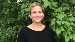Aino Sarkia hymyilee kameralle ulkona. Taustalla vehreä puu.
