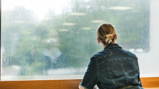 Tyttö nojaa pöytään ja katsoo ulos ikkunasta.