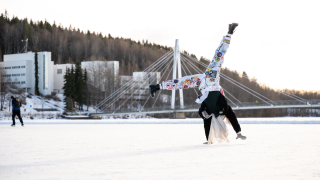 Opiskelija tekee kärrynpyörän järven jäällä, taustalla Ylistön silta ja kampusta. 