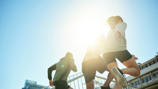 Kolme urheilijaa juoksevat portaita ylös aurinkoisella kelillä.