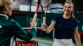Kaksi naispelaajaa tenniskentällä.