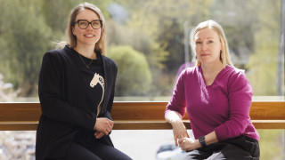 Jenni Virtaluoto ja Laura Pajula istuvat ja hymyilevät kameralle.