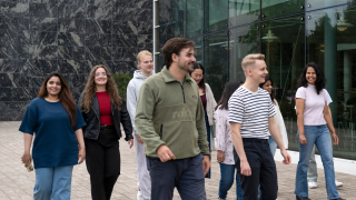 Opiskelijoita kävelee yliopistorakennuksen edustalla. 