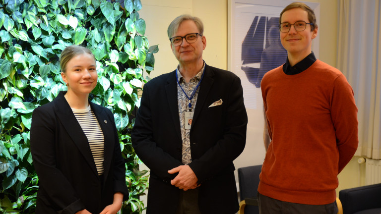 Ylioppilaskunnan hallituksen puheenjohtaja Venla Suosalo, rehtori Jari Ojala ja ylioppilaskunnan toiminnanjohtaja Teemu Vasama seisovat rehtorin toimistossa, katsovat hymyillen kameraan.