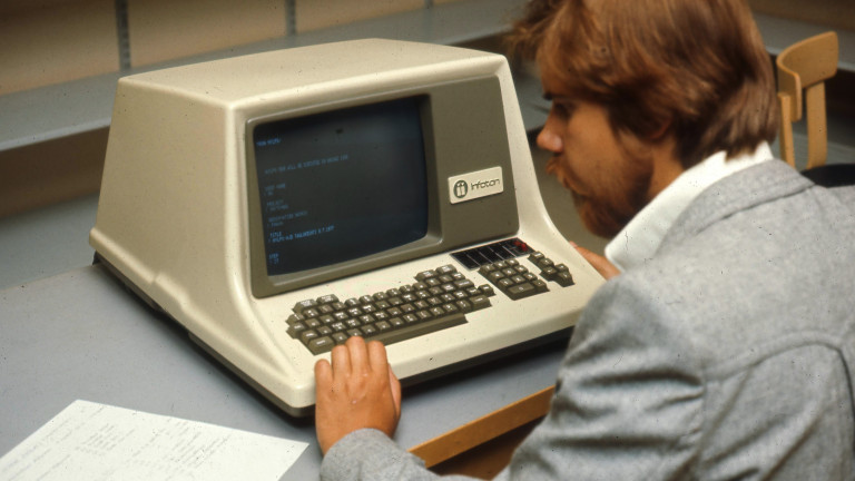 An old photograph where a man sits in front of an early model of a computer