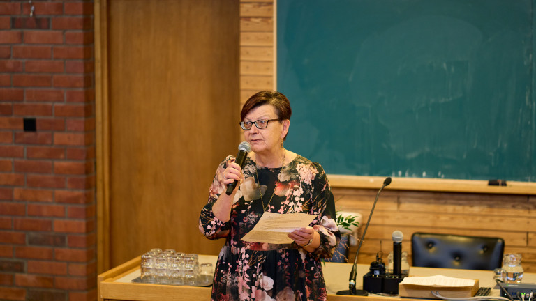 Marjo Kuronen puhuu mikkiin. Taustalla tummanvihreä liitutaulu.