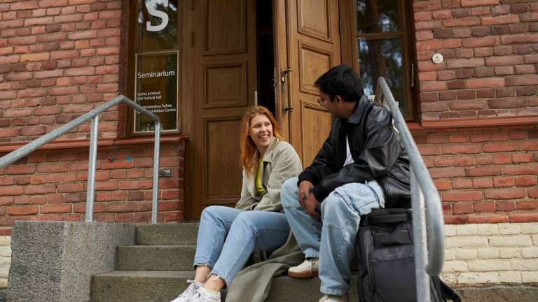Kaksi opiskelijaa istuu S-rakennuksen portailla