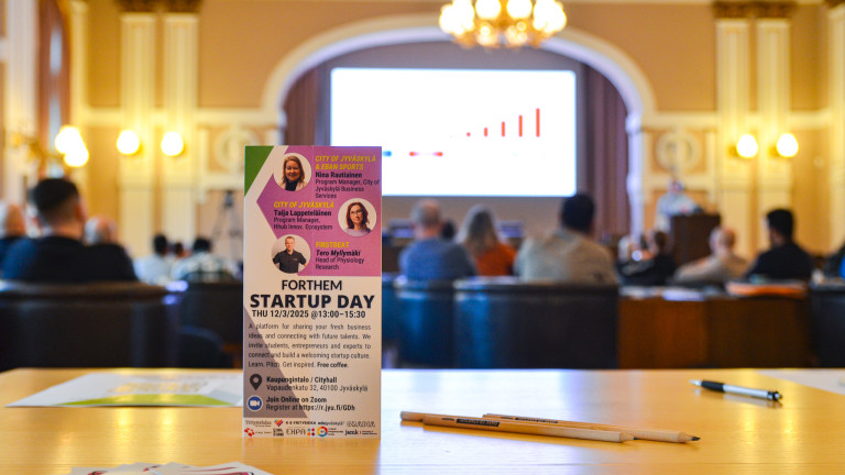 Forthem Startup Day marketing material on a table with entrepreneurship pencils and stickers, behind an audience listening to a presentation