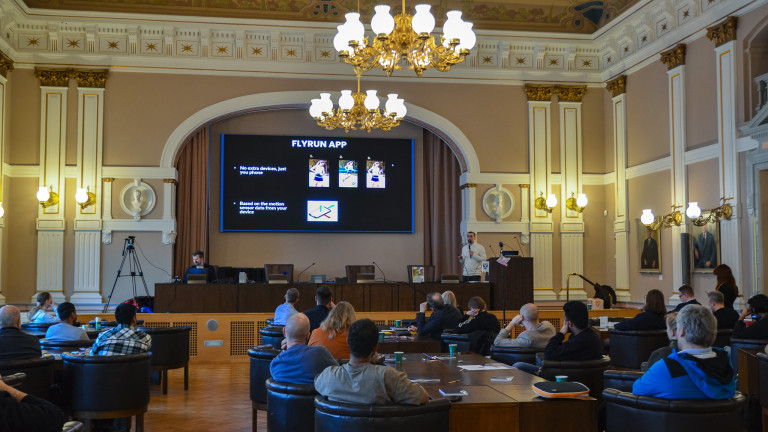 A presentation in the Great Hall in the Jyväskylä City Hall, screen showing white "Flyrun App, no extra devices, just your phone" text on a black background