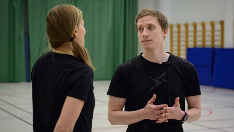 Kaksi henkilöä keskustelee liikuntasalissa 
