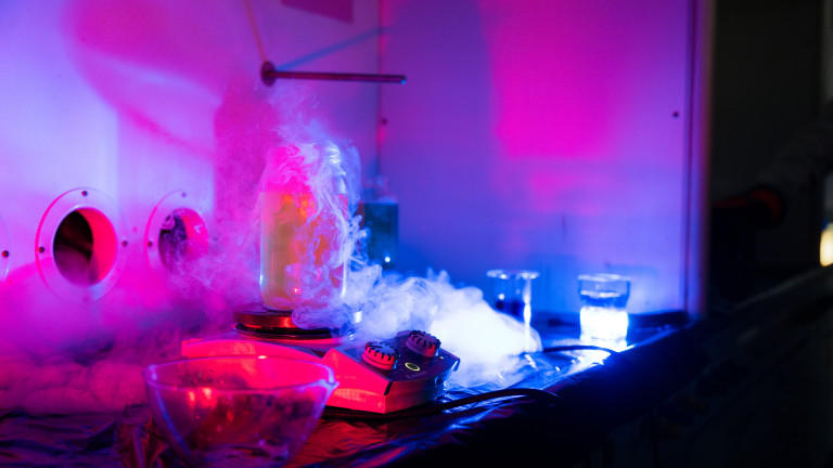 Tutkijoiden yön työpajan laboratorionäytös, jossa lasiastiasta nousee valkoista savua neonvalaistuksessa.
