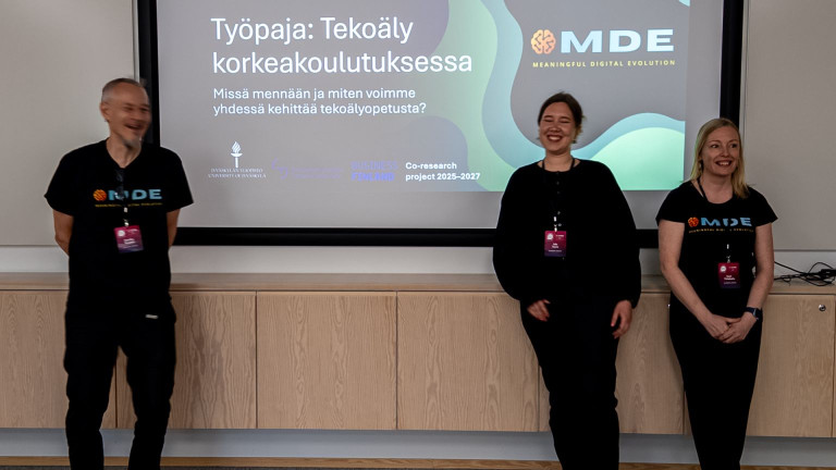 Kolme ihmistä seisoo valkokankaan edessä pitämässä työpajaa