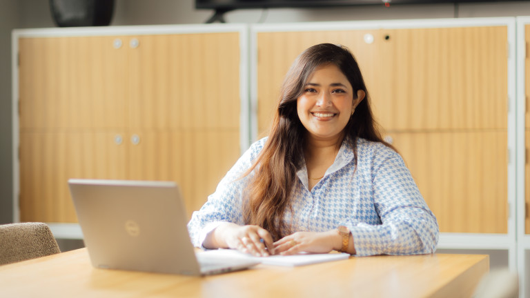 A woman studying on computer at the University and smiling to the camera.