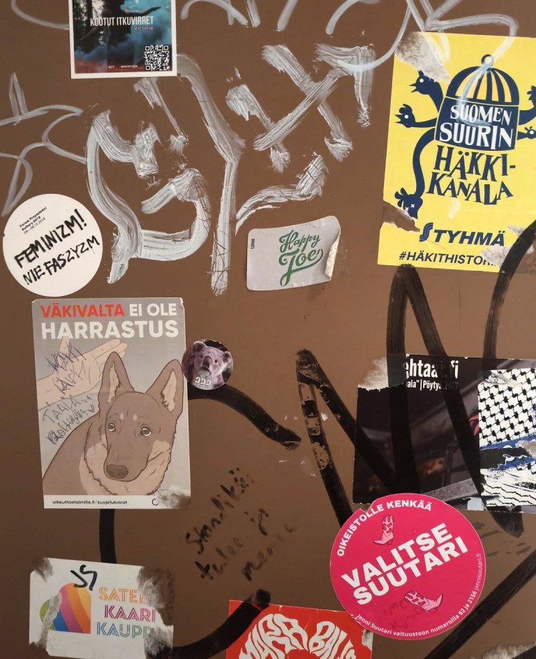 Erilaisia kantaaottavia tarroja vessanovessa, kuten kuva koiran lyömisestä tekstillä Väkivalta ei ole harrastus